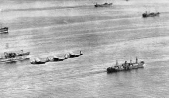 Una escolta de hidroaviones antisubmarinos sobrevuela un Liberty Ship de proa a popa
