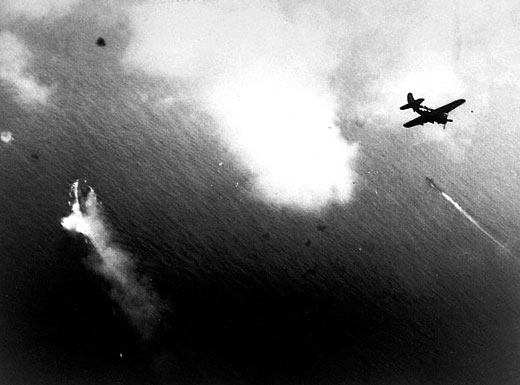 Un avión norteamericano sobrevuela al IJN Yamato durante al ataque. Son visibles las detonaciones de las baterías antiaéreas y un destructor de escolta
