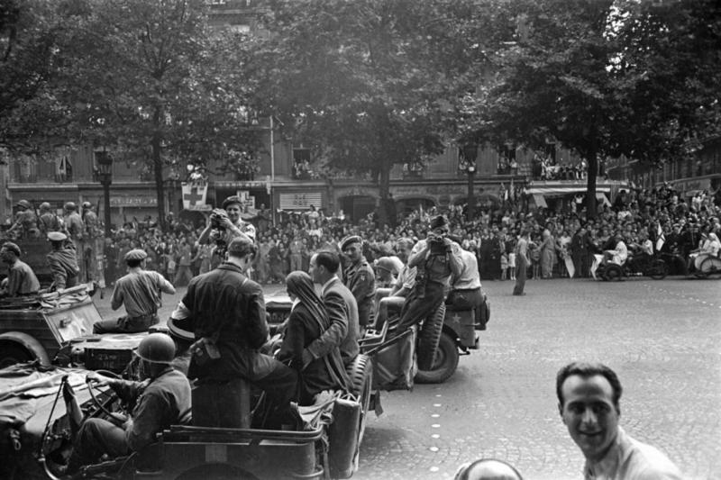 Soldados aliados y periodistas - entre ellos los fotógrafos Robert Capa, en la parte trasera de un jeep con una cámara en la cara y George Rodger, con una cámara y portando una boina, que ayudaron a fundar el colectivo Magnum- en las calles de París durante la liberación de la ciudad, agosto de 1944