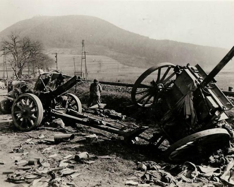 Un soldado de EE.UU. contempla dos cañones nazis destruidos. Junto a él yace el cadáver un militar alemán