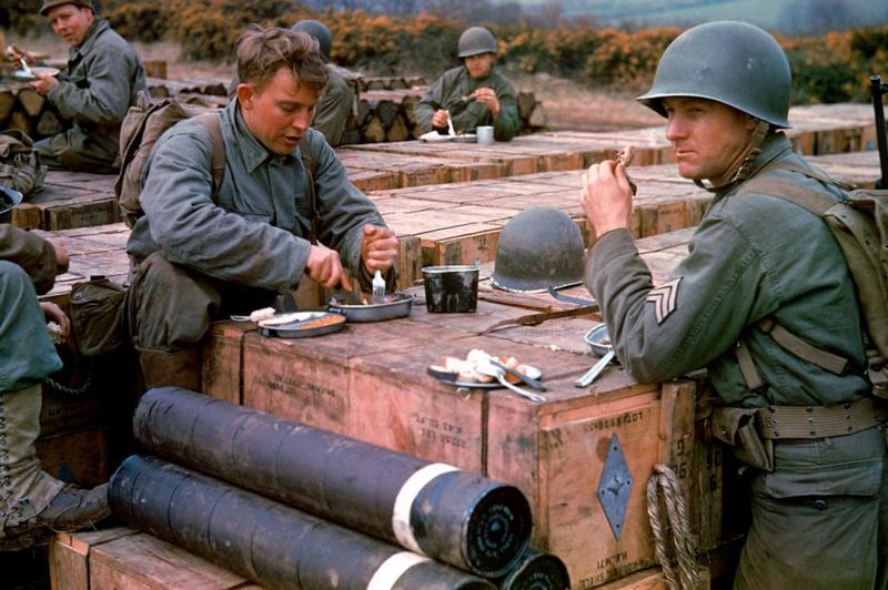 Ingenieros estadounidenses comen encima de cajas de municiones almacenadas para la inminente invasión del Día D, mayo de 1944